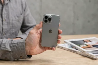 Main tenant un iPhone 15 Pro avec une coque transparente compatible MagSafe sur un bureau en bois minimaliste